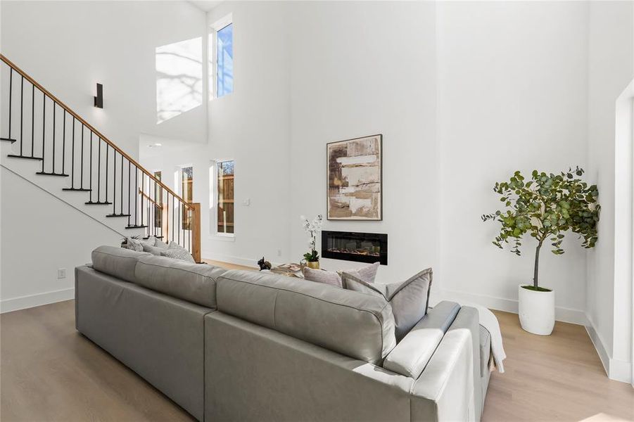Living area with a glass covered fireplace, light wood-style floors, stairway, and a high ceiling