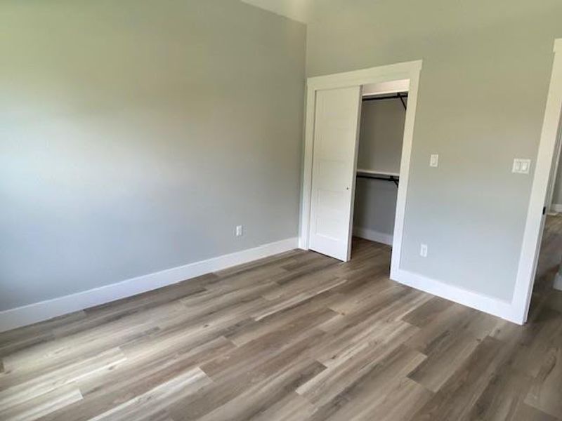 A well-lit bedroom featuring durable plank flooring and a convenient sliding closet door. A well-lit bedroom featuring durable plank flooring and a convenient sliding closet door.