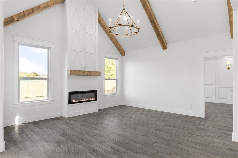 Unfurnished living room with high vaulted ceiling, beamed ceiling, a large fireplace, dark hardwood / wood-style flooring, and a chandelier