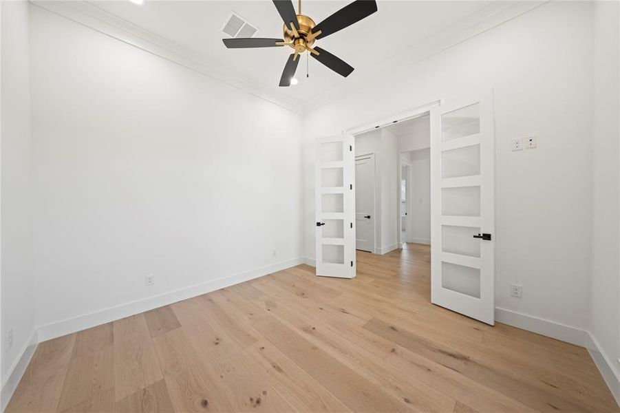 Light wood-finish flooring featuring a gold and black ceiling fan and crown molding