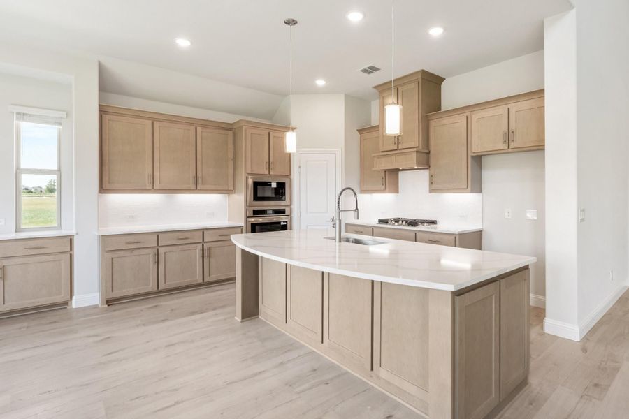 Kitchen with light wood cabinets, large center island with white countertop, and pendant lights overhead