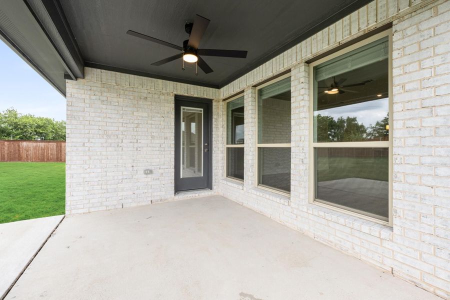 Covered back patio with ceiling fan, white brick exterior, gray door, and concrete floor overlooking fenced backyard Covered back patio with ceiling fan, white brick exterior, gray door, and concrete floor overlooking fenced backyard