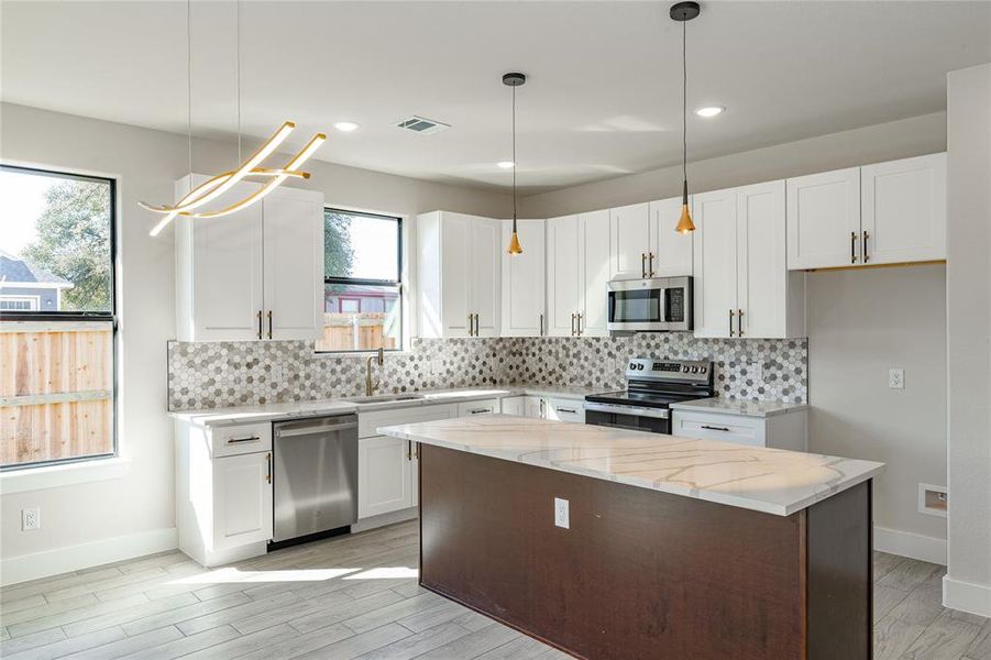 Kitchen with appliances with stainless steel finishes, white cabinetry, and a kitchen island