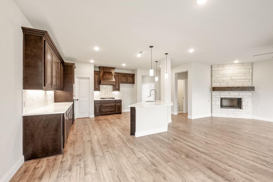 Open-concept kitchen and living area with dark wood cabinets, white island, hardwood floors, and stone fireplace.