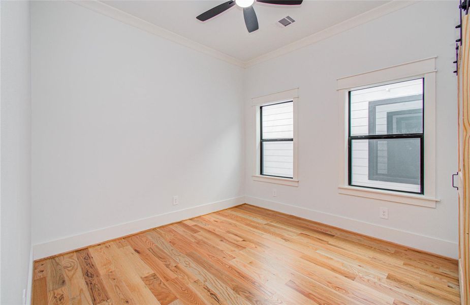 This bright secondary bedroom features hardwood floors, two large windows for natural light, and a stylish sliding barn door.