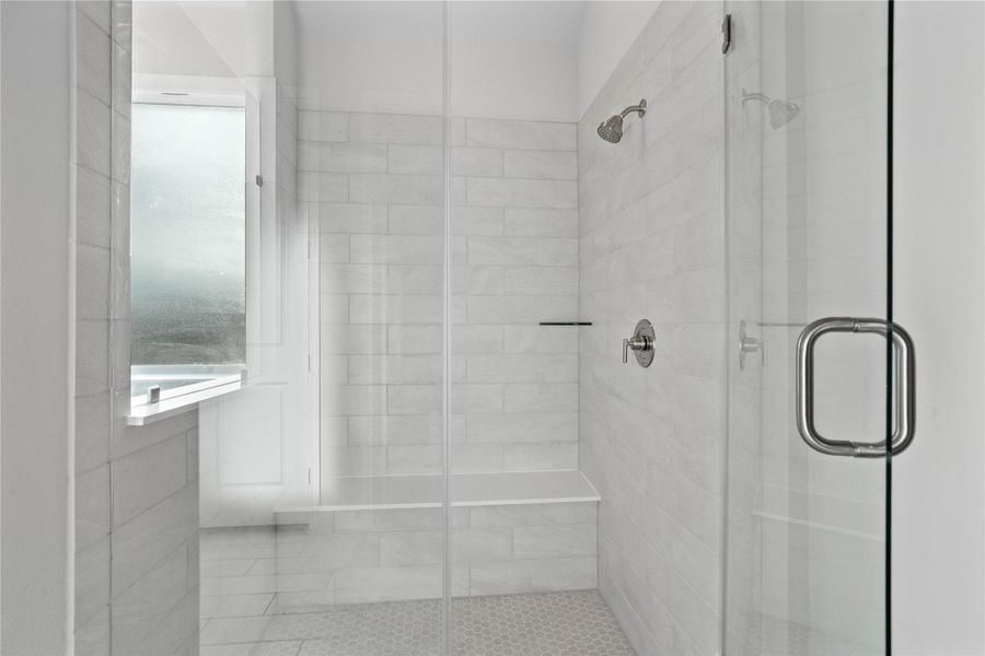 The walk-in shower includes a convenient, integrated bench with a shelf, offering comfort, extra storage space, and a high-end, custom appearance.