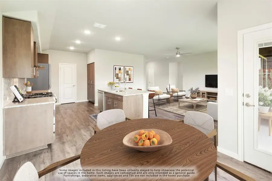 Open-plan dining area with round wood table, kitchen island, and living room with hardwood floors