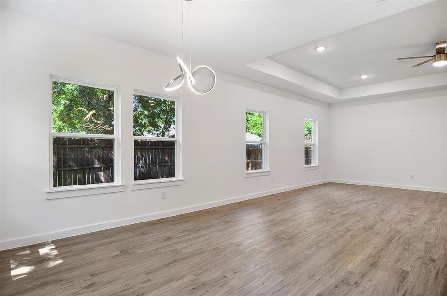 Empty room with ceiling fan with notable chandelier, hardwood / wood-style flooring, and a tray ceiling