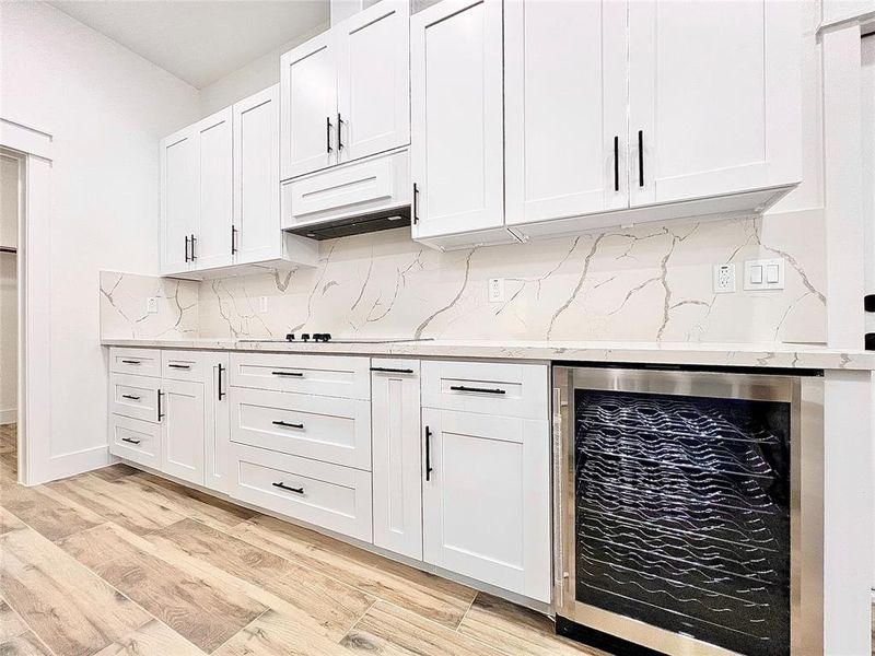 Kitchen offers a Beautiful Stainless Steal Wine Cooler and Clean Modern White Shaker Cabinets with Black Hardware.