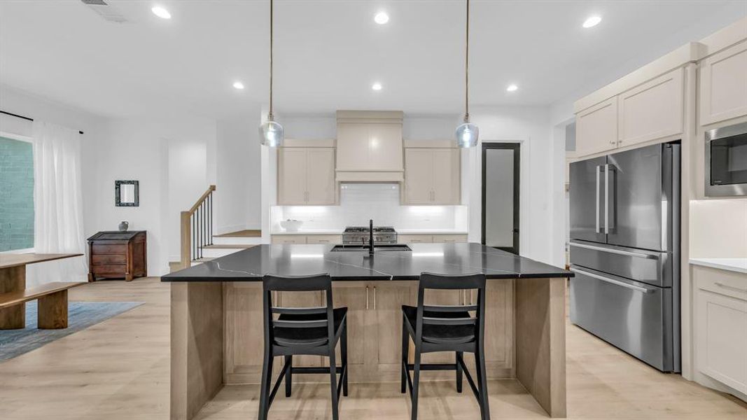 Kitchen featuring high end appliances, custom exhaust hood, backsplash, light wood-style flooring, and a kitchen breakfast bar Kitchen featuring high end appliances, custom exhaust hood, backsplash, light wood-style flooring, and a kitchen breakfast bar