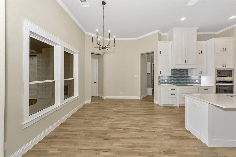 Kitchen with white cabinets, light hardwood / wood-style floors, ornamental molding, stovetop, and a chandelier