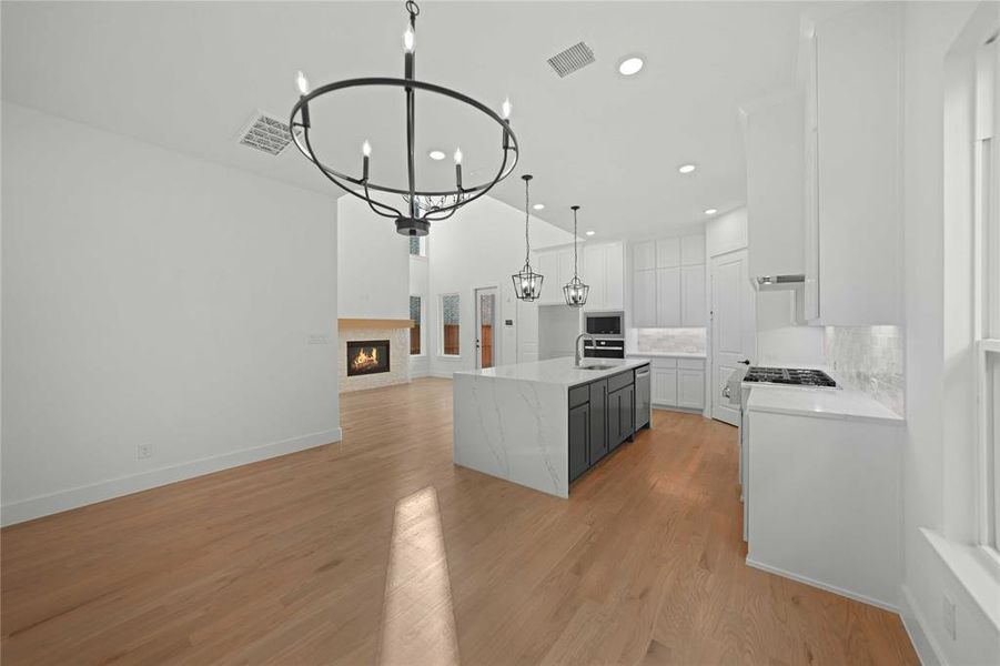 Kitchen featuring white cabinets, decorative light fixtures, light stone countertops, open floor plan, and a chandelier Kitchen featuring white cabinets, decorative light fixtures, light stone countertops, open floor plan, and a chandelier