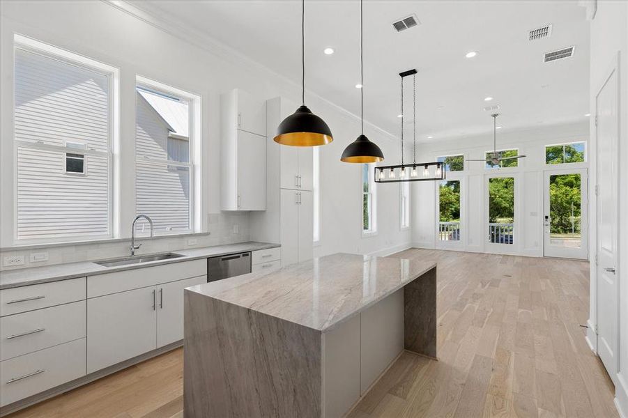 Open-concept kitchen and living area featuring a waterfall island with stone countertop, stainless steel sink, and white cabinetry