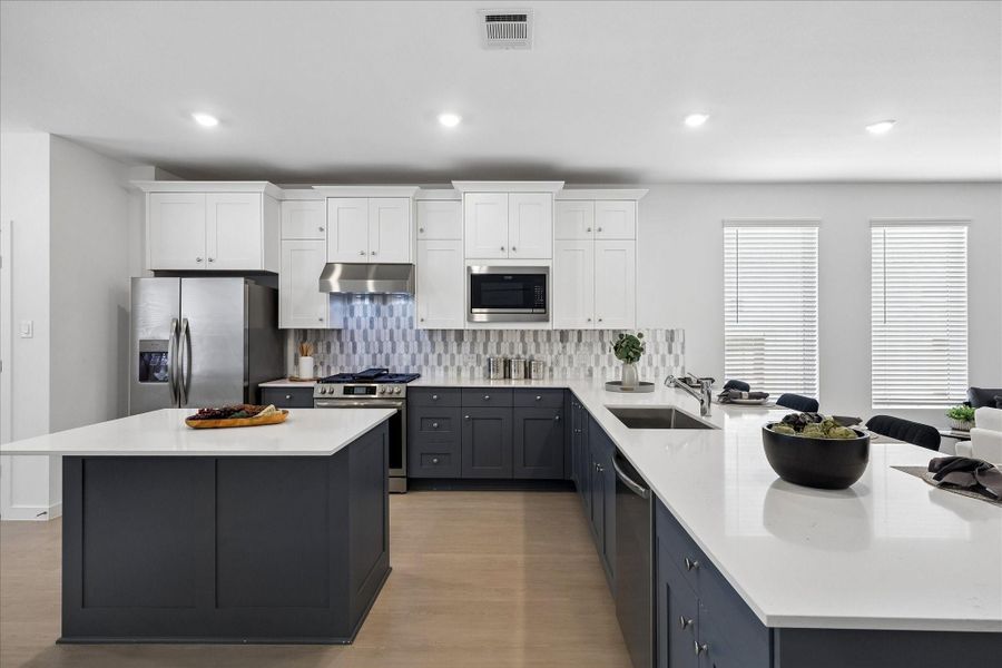 Designed to work as beautifully as it looks, this spacious kitchen pairs quartz countertops and a designer tile backsplash with crisp white upper cabinetry, contrasting lower cabinets and stainless steel appliances. A center island adds extra prep space, while the long bar with a deep basin stainless steel sink offers plenty of room to serve, seat and gather.