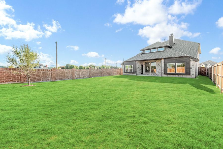 Backyard with large green lawn, brick and wood privacy fence, and two-story home with stone exterior Backyard with large green lawn, brick and wood privacy fence, and two-story home with stone exterior