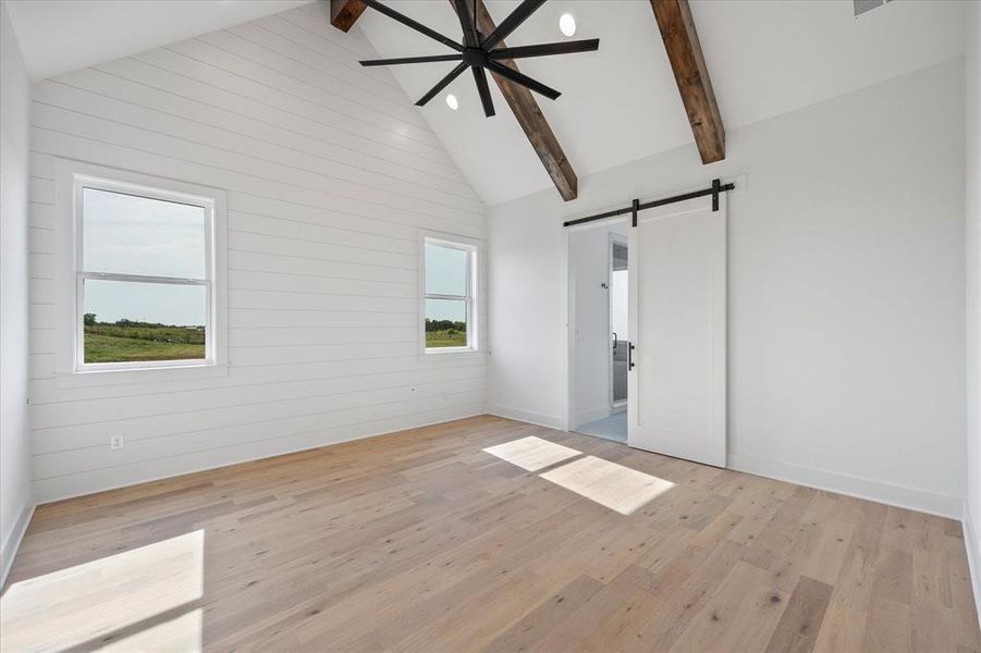 Prinary Bedroom featuring a barn door, high vaulted ceiling, light wood-style flooring, beamed ceiling, and wood walls Prinary Bedroom featuring a barn door, high vaulted ceiling, light wood-style flooring, beamed ceiling, and wood walls