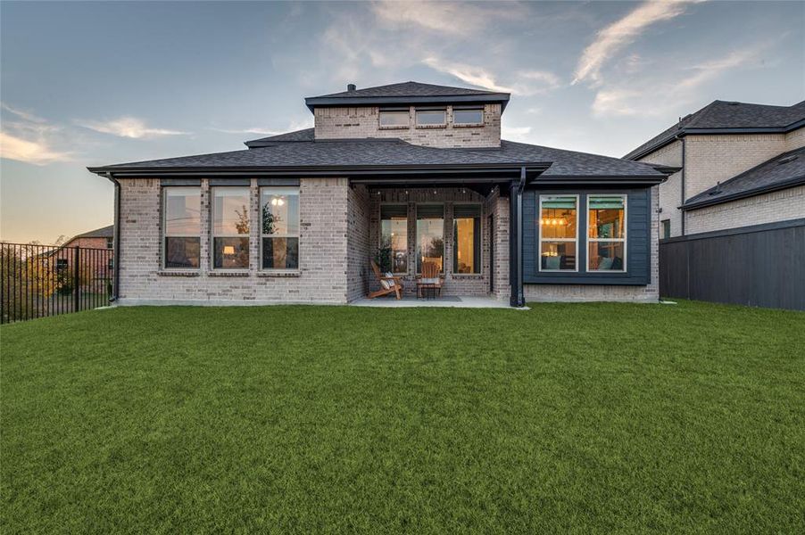 Back of house at dusk featuring a fenced backyard, brick siding, a patio area, and roof with shingles