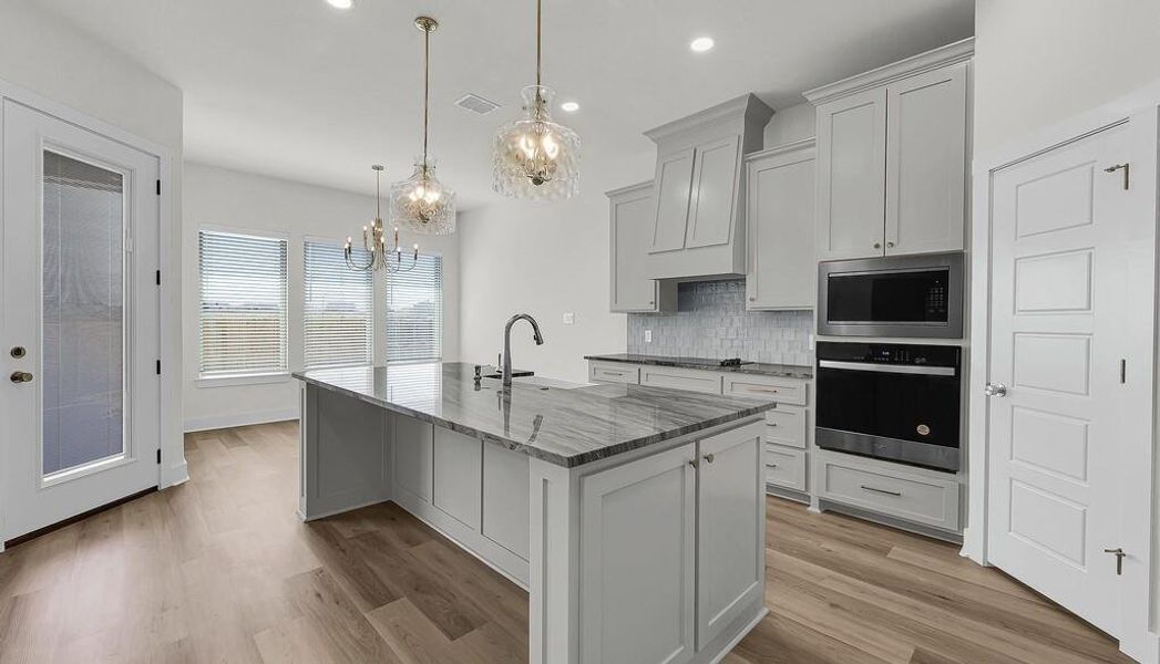 Kitchen featuring backsplash, black appliances, light wood-style floors, dark stone countertops, and decorative light fixtures