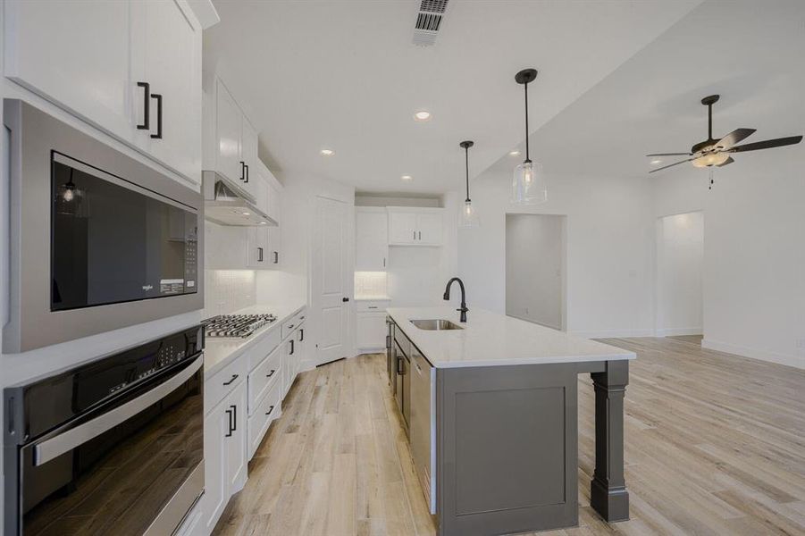 Modern kitchen featuring white cabinetry, stainless steel appliances, a center island with a sink, pendant lighting, and wood-finish flooring