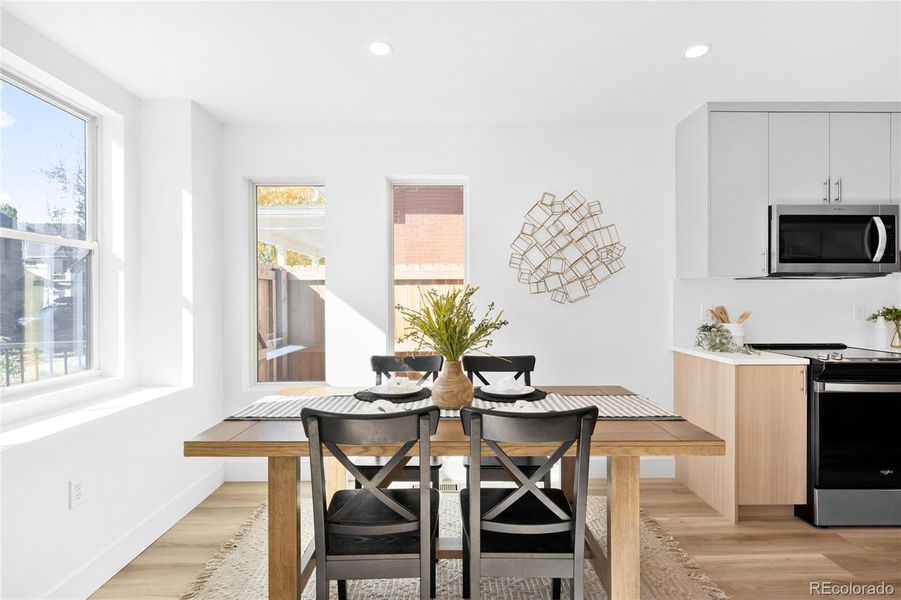 Sunlit dining area flows seamlessly into a modern kitchen with sleek cabinetry and warm wood tones.