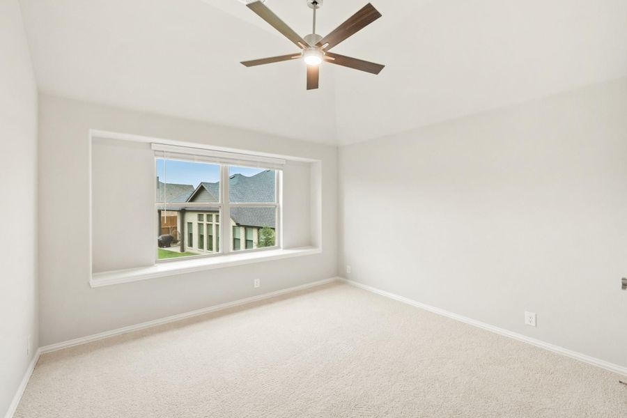 Empty bedroom with carpet flooring, ceiling fan, and large window overlooking neighboring homes Empty bedroom with carpet flooring, ceiling fan, and large window overlooking neighboring homes