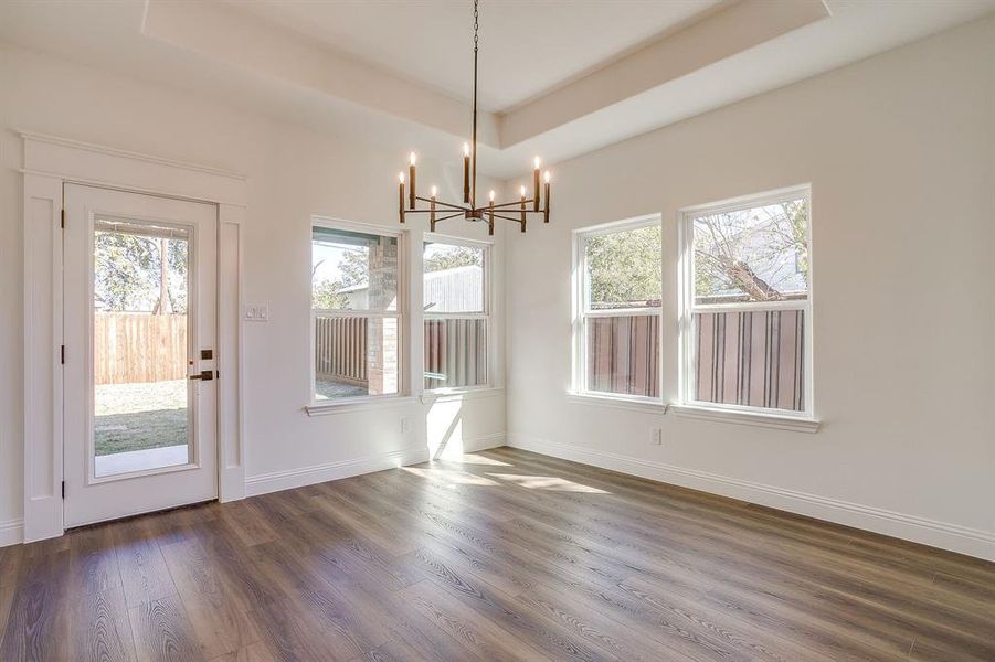 Unfurnished dining area with dark wood-type flooring, a tray ceiling, and a chandelier