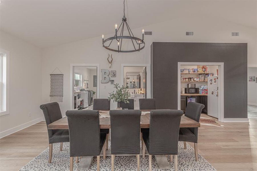 Dining space with vaulted ceiling, a chandelier, and light wood-style flooring