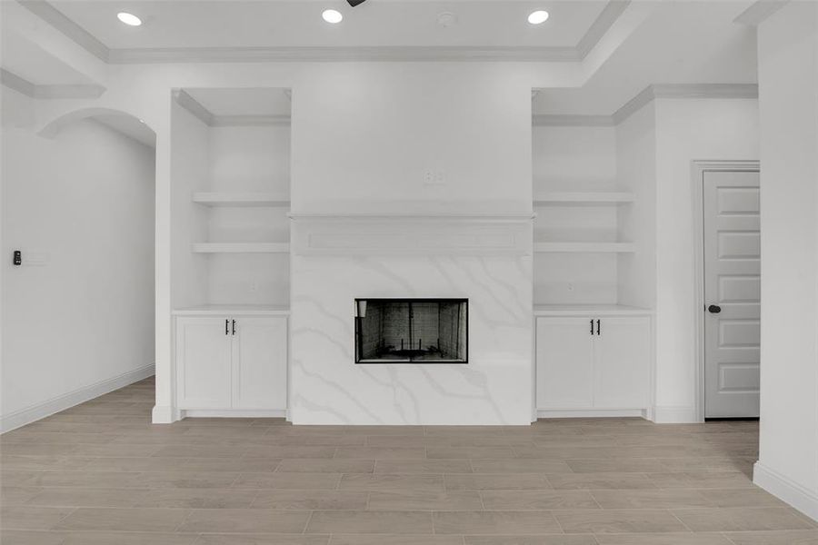 Unfurnished living room featuring built in shelves, ornamental molding, recessed lighting, a premium fireplace, and light wood-type flooring Unfurnished living room featuring built in shelves, ornamental molding, recessed lighting, a premium fireplace, and light wood-type flooring
