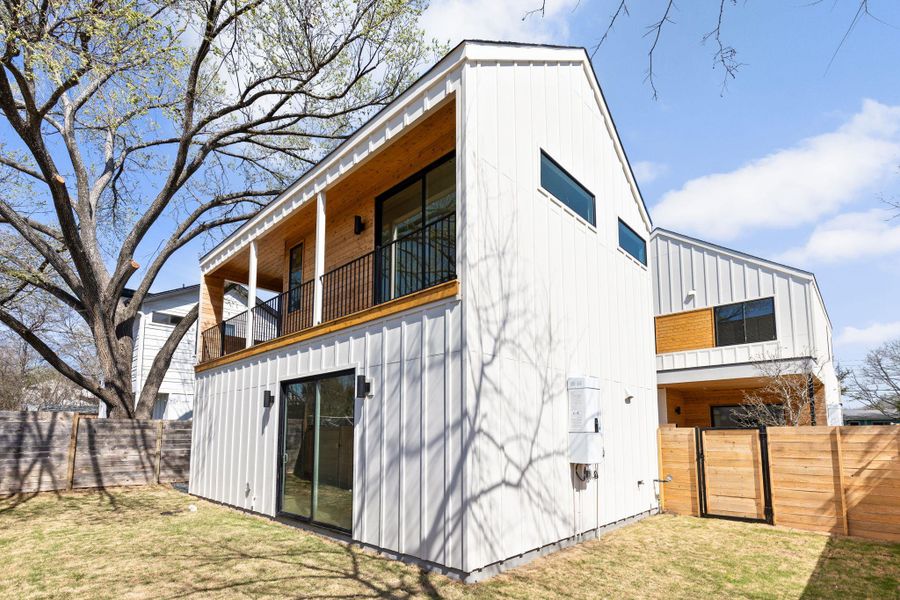 Back of property featuring a lawn, a gate, a fenced backyard, board and batten siding, and a balcony