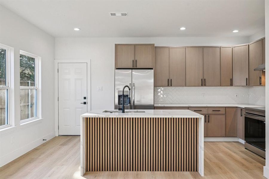 Kitchen with light stone counters, stainless steel appliances, light wood-style flooring, a center island with sink, and recessed lighting