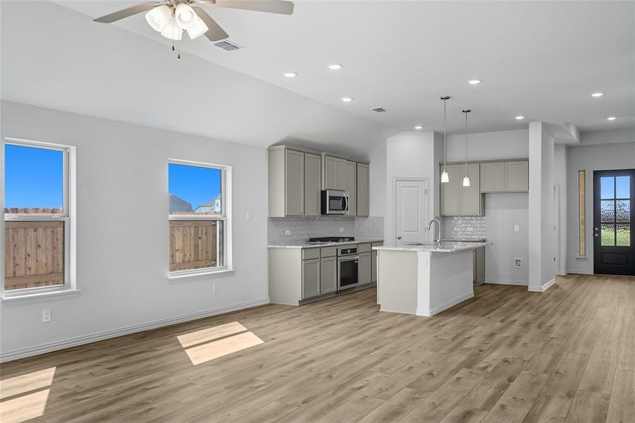Kitchen with gray cabinets, decorative backsplash, a center island with sink, lofted ceiling, and hanging light fixtures Kitchen with gray cabinets, decorative backsplash, a center island with sink, lofted ceiling, and hanging light fixtures