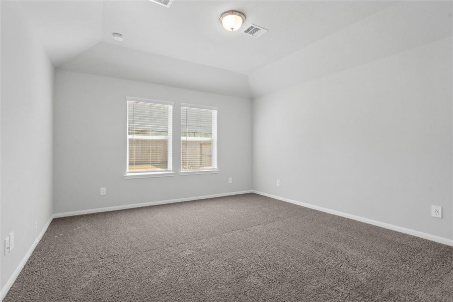 The primary bedroom provides a peaceful escape with a bright, neutral palette, sloped ceilings, large windows (fitted with blinds), and plush carpet flooring, creating a calm and restorative atmosphere to end your day.