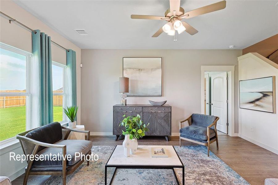 Living area featuring wood-finish flooring, a ceiling fan with integrated lighting, and multiple windows