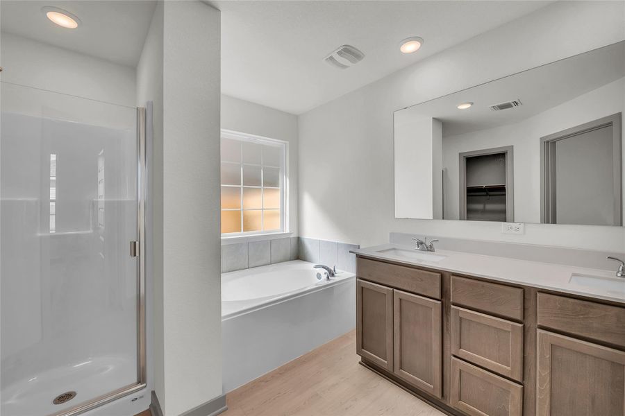 Full bathroom featuring double vanity, a shower stall, a spacious closet, a bath, and light wood finished floors