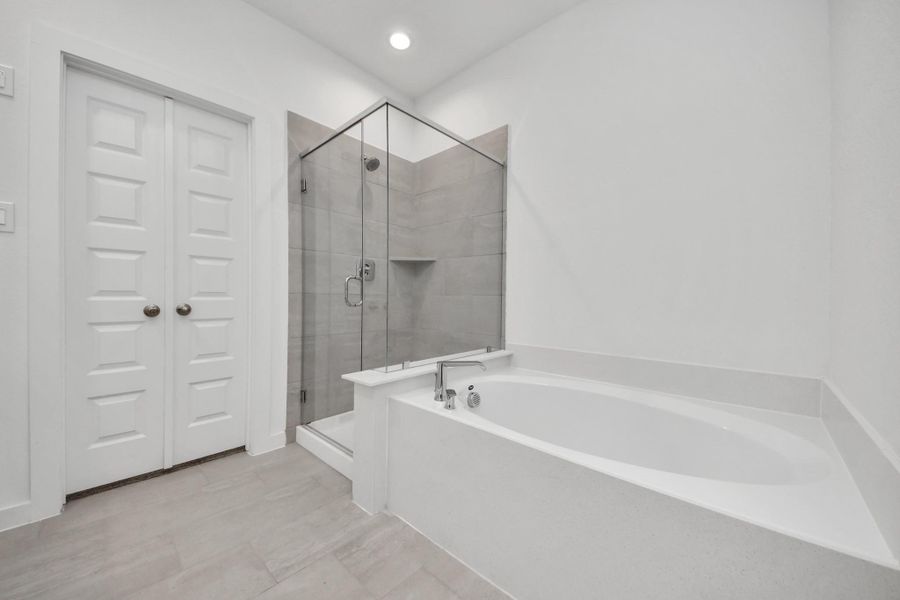Indulge in a spa-like retreat within the confines of this primary bathroom. Delight in a spacious walk-in shower enveloped in stylish tile surround, unwind in a separate garden tub adorned with custom detailing. Sample photo of completed home with similar floor plan. Actual colors and selections may vary.