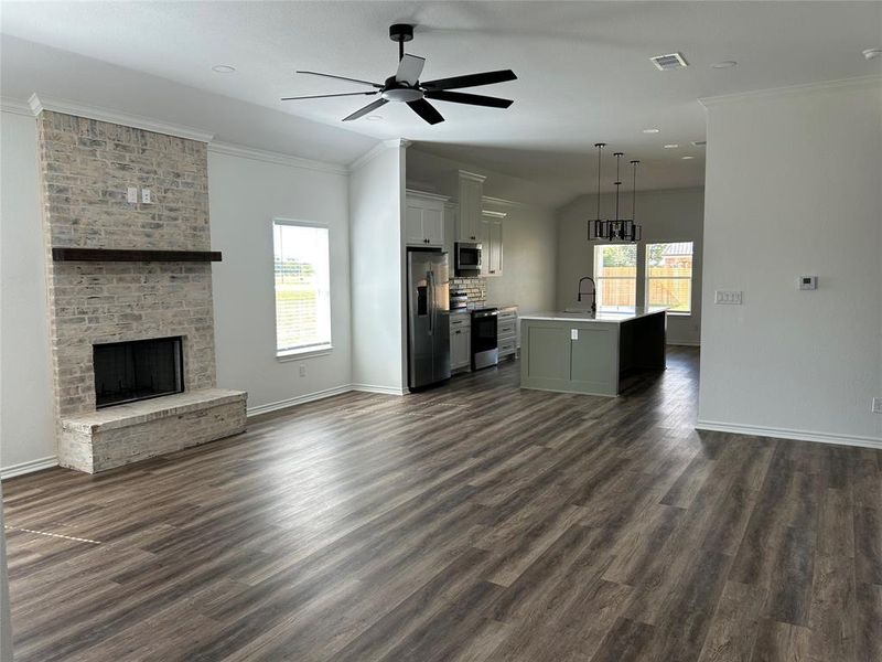 Unfurnished living room with ornamental molding, a brick fireplace, ceiling fan, dark wood-type flooring, and vaulted ceiling