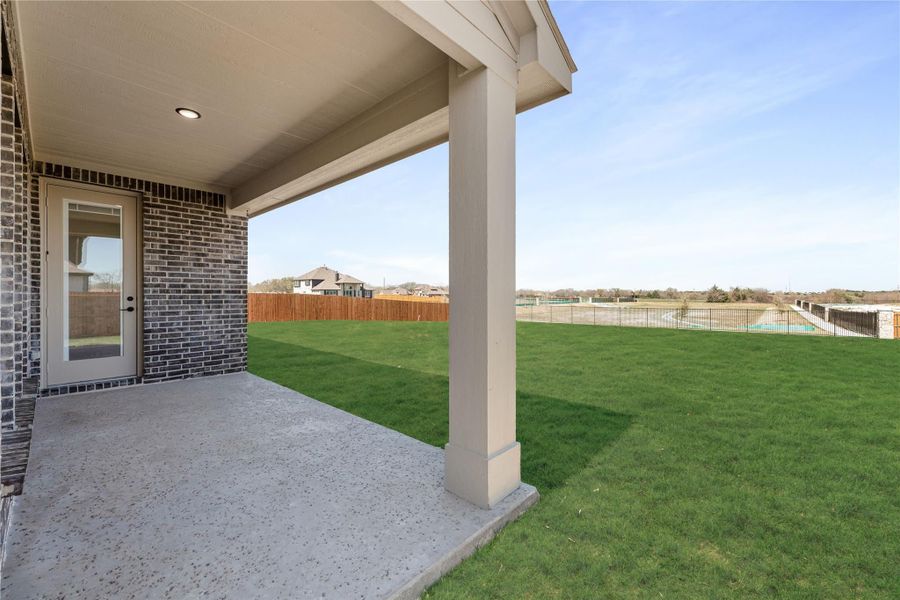 Covered back patio with concrete floor overlooking large grassy yard with wood fence and pool area beyond. Covered back patio with concrete floor overlooking large grassy yard with wood fence and pool area beyond.