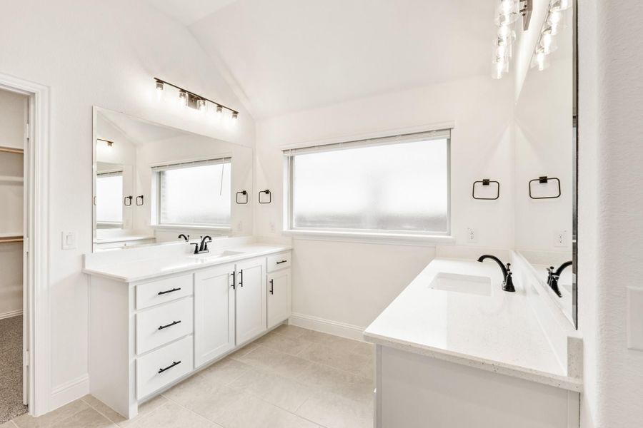 Master bathroom with white double vanity, soaking tub, black hardware, and tile floors