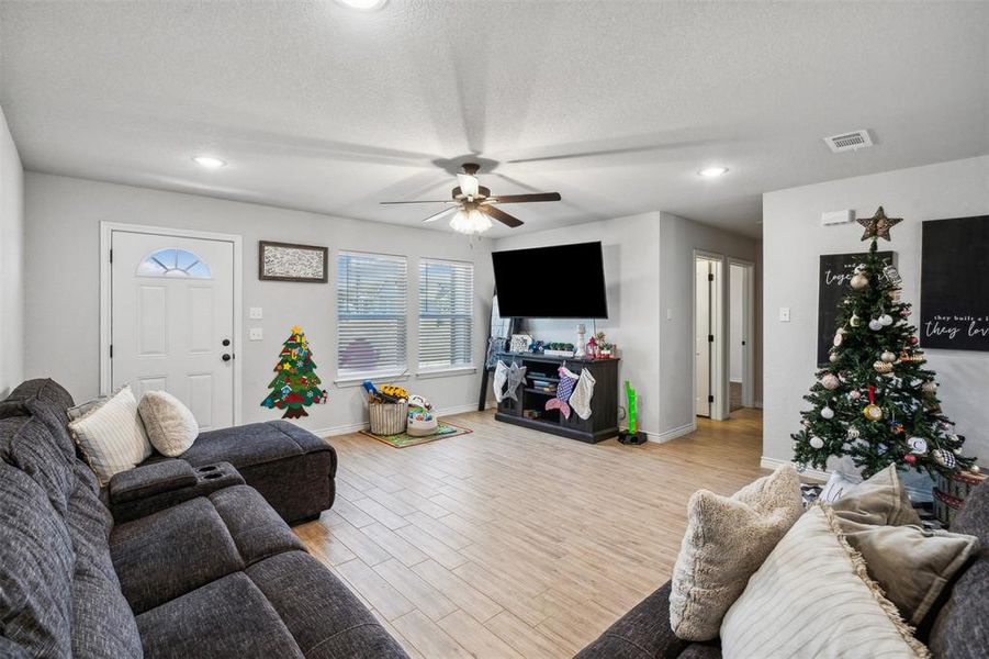 Living room with a textured ceiling, light hardwood / wood-style flooring, and ceiling fan