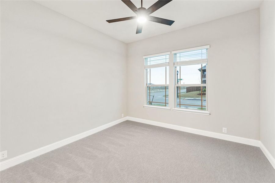 Empty bedroom with gray carpet, ceiling fan, and two windows with street view