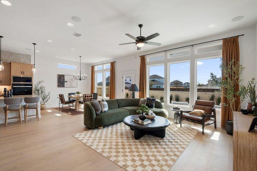 Open-concept living area featuring light wood-finish flooring, a contemporary ceiling fan, and large windows with transom panels