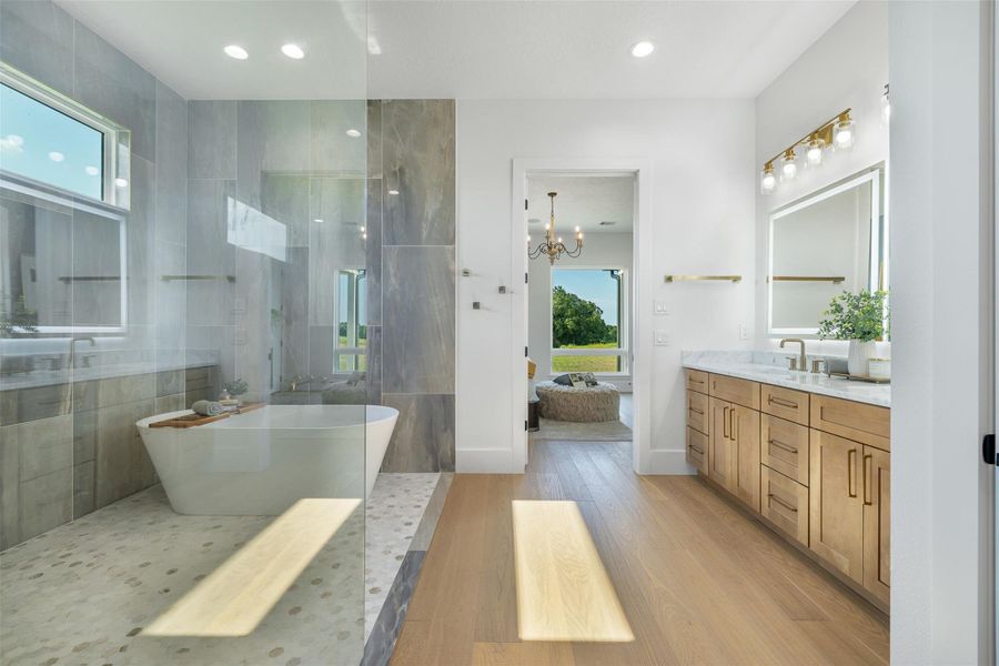 Full bath wet area featuring light wood finished floors, a walk in shower, a freestanding tub, vanity, and a chandelier