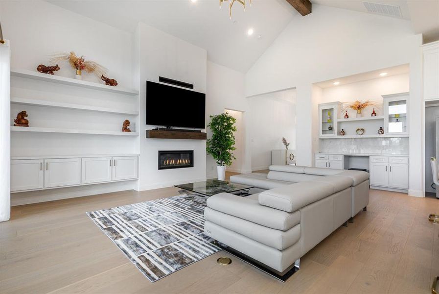 Living area featuring built in features, a glass covered fireplace, high vaulted ceiling, light wood-style floors, and beamed ceiling