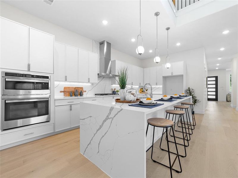 Kitchen featuring light wood-type flooring, tasteful backsplash, a large island with sink, stainless steel double oven, and white cabinets