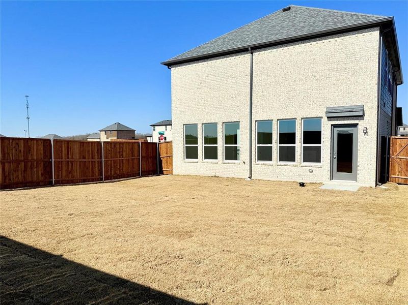 Rear view of property featuring a shingled roof, a fenced backyard, and brick siding