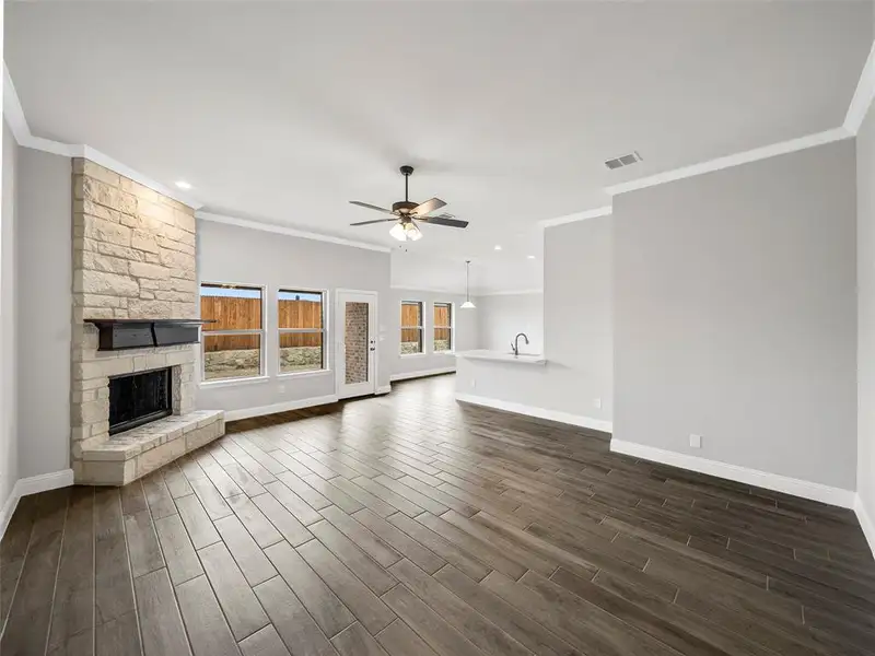 Unfurnished living room featuring a stone fireplace, ceiling fan, baseboards, ornamental molding, and dark wood-type flooring