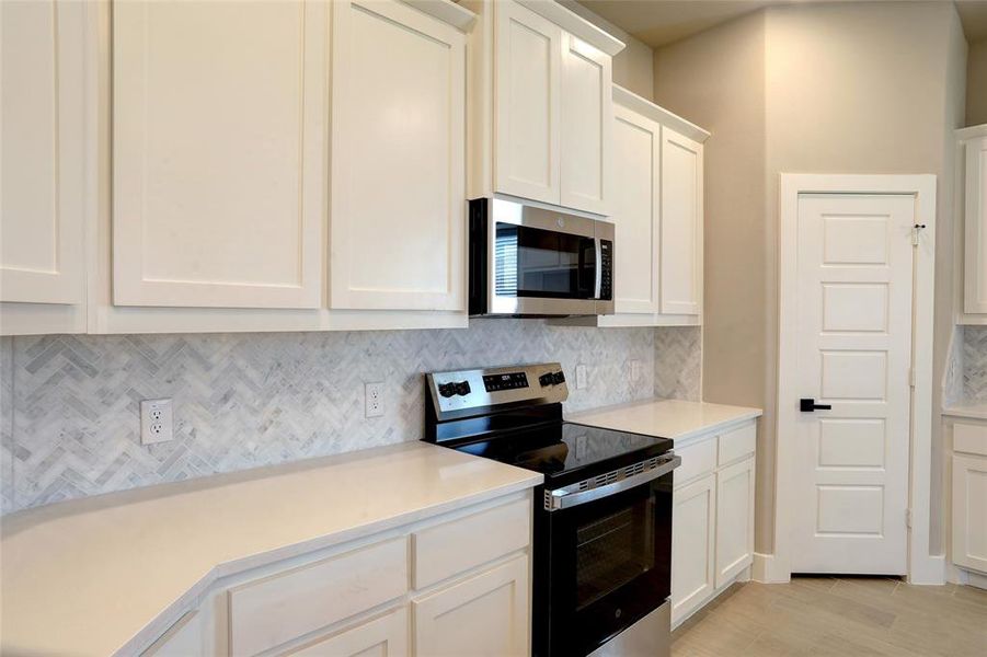 Kitchen with stainless steel appliances, decorative backsplash, white cabinetry, light wood-type flooring, and light stone counters Kitchen with stainless steel appliances, decorative backsplash, white cabinetry, light wood-type flooring, and light stone counters