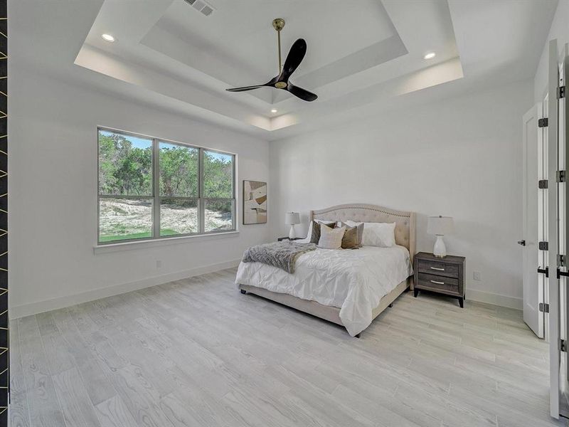 Bedroom with a raised ceiling, light wood-style floors, recessed lighting, and a ceiling fan