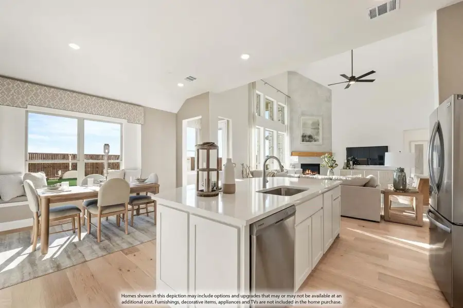 Open-concept kitchen with white island, stainless appliances, and views into dining and living areas with fireplace and vaulted ceiling.
