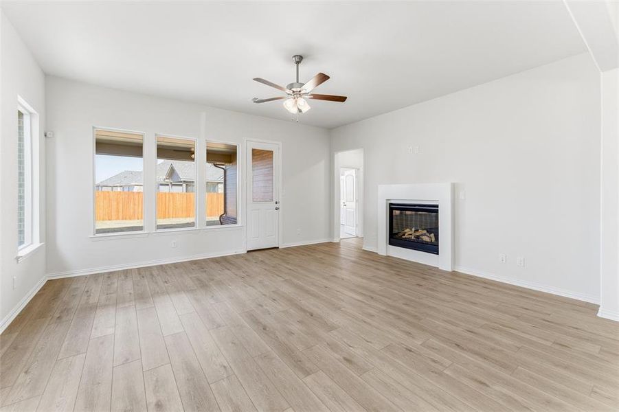 Unfurnished living room featuring a glass covered fireplace, light wood-type flooring, and ceiling fan Unfurnished living room featuring a glass covered fireplace, light wood-type flooring, and ceiling fan